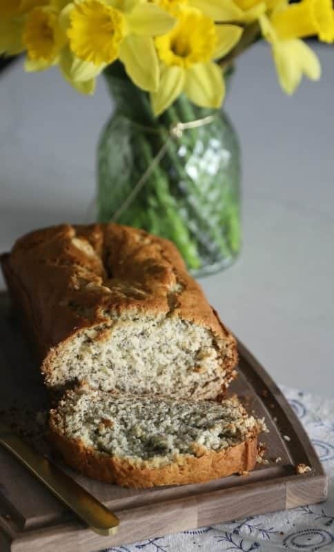 moist banana bread sliced on a wood cutting board with daffodils in a vase in the background