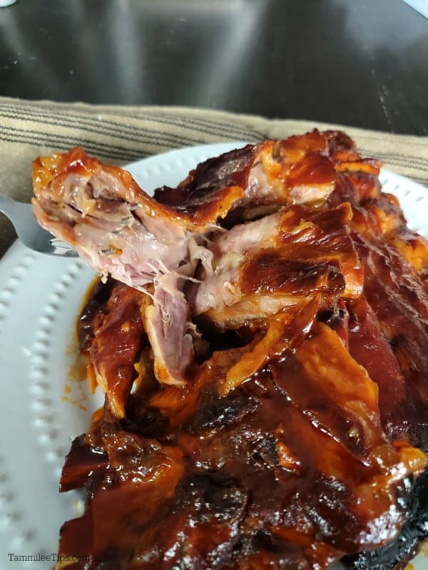 Fork pulling meat off of crockpot ribs on a white plate