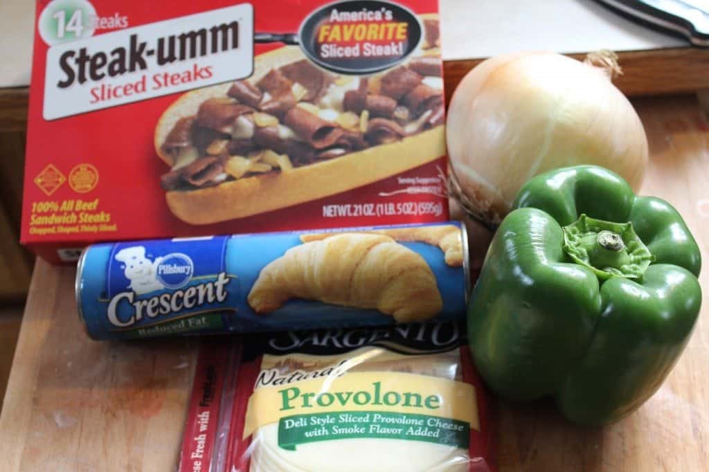 steak umm, crescent rolls, provolone cheese, onion, and green pepper on a cutting board. 