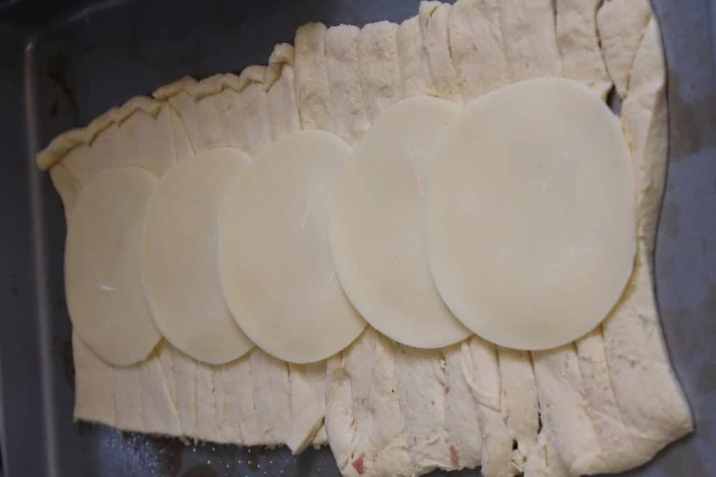 Provolone Cheese spread down a roll of crescent dough on a baking sheet