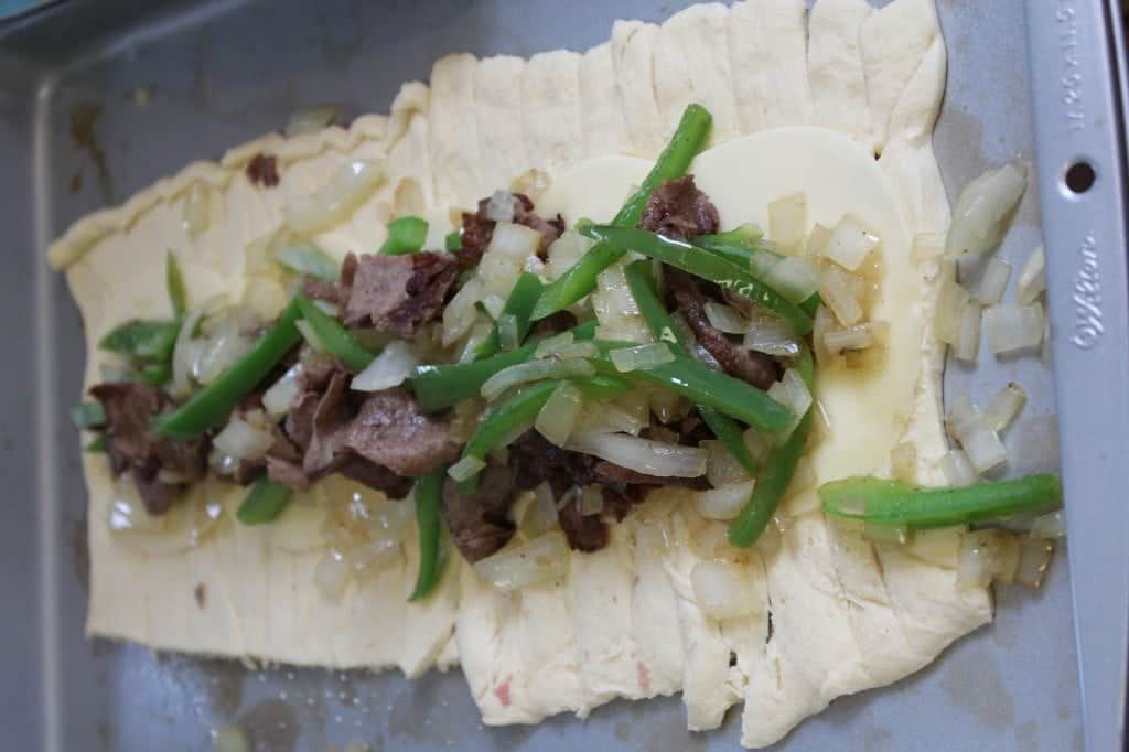 cheesesteak, peppers, and onions on top of crescent dough on a baking sheet