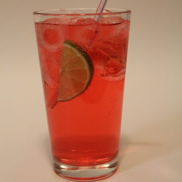 cherry limeade in a tall glass with a lime wedge and straw