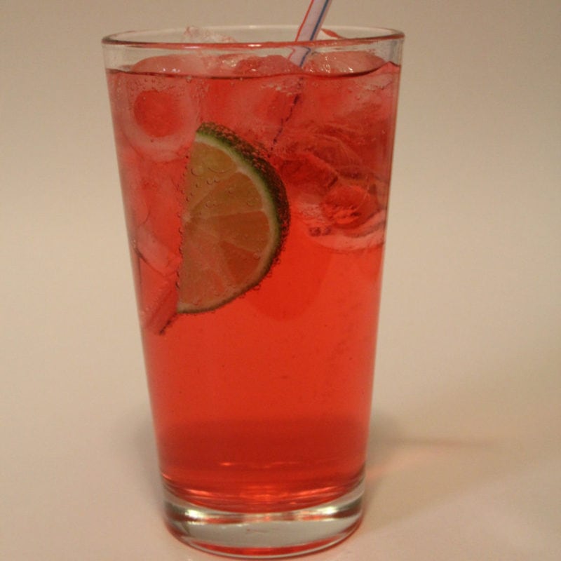 cherry limeade in a tall glass with a lime wedge and straw