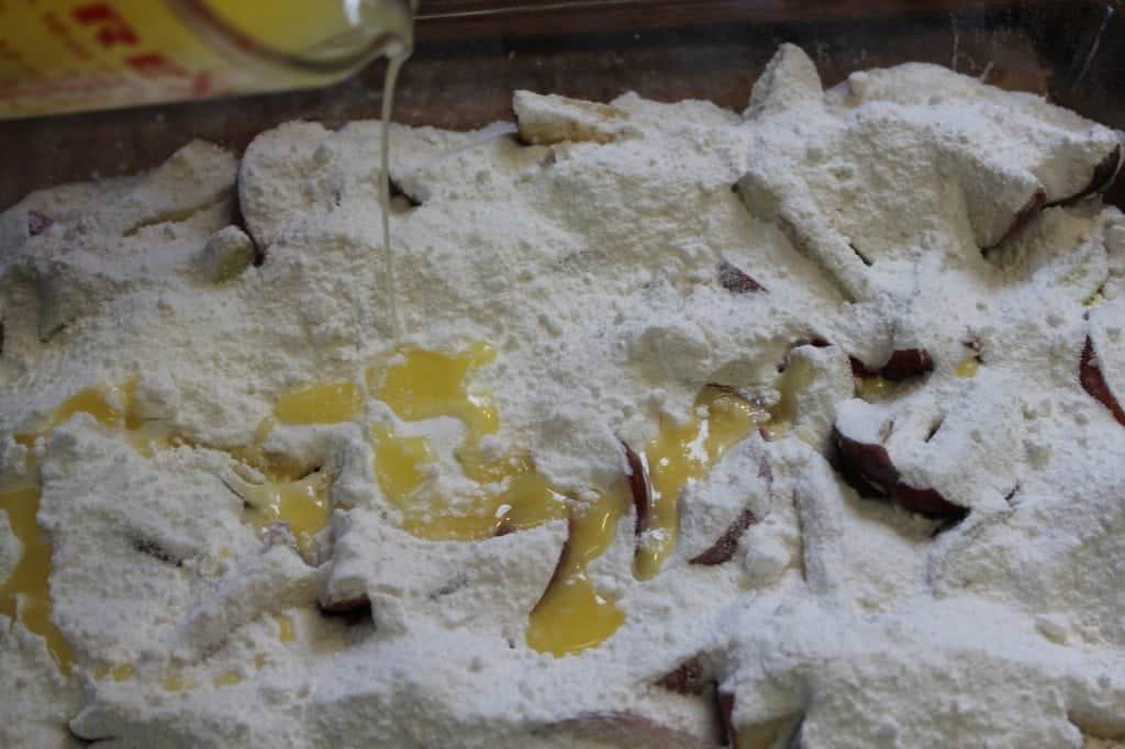 Melted butter pouring over dry cake mix and apples