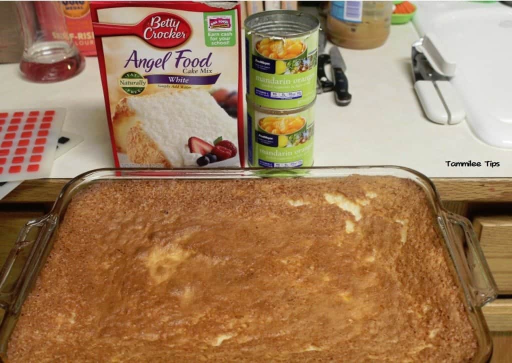 Angel food cake mix, two cans of mandarin oranges on a counter next to a cake 