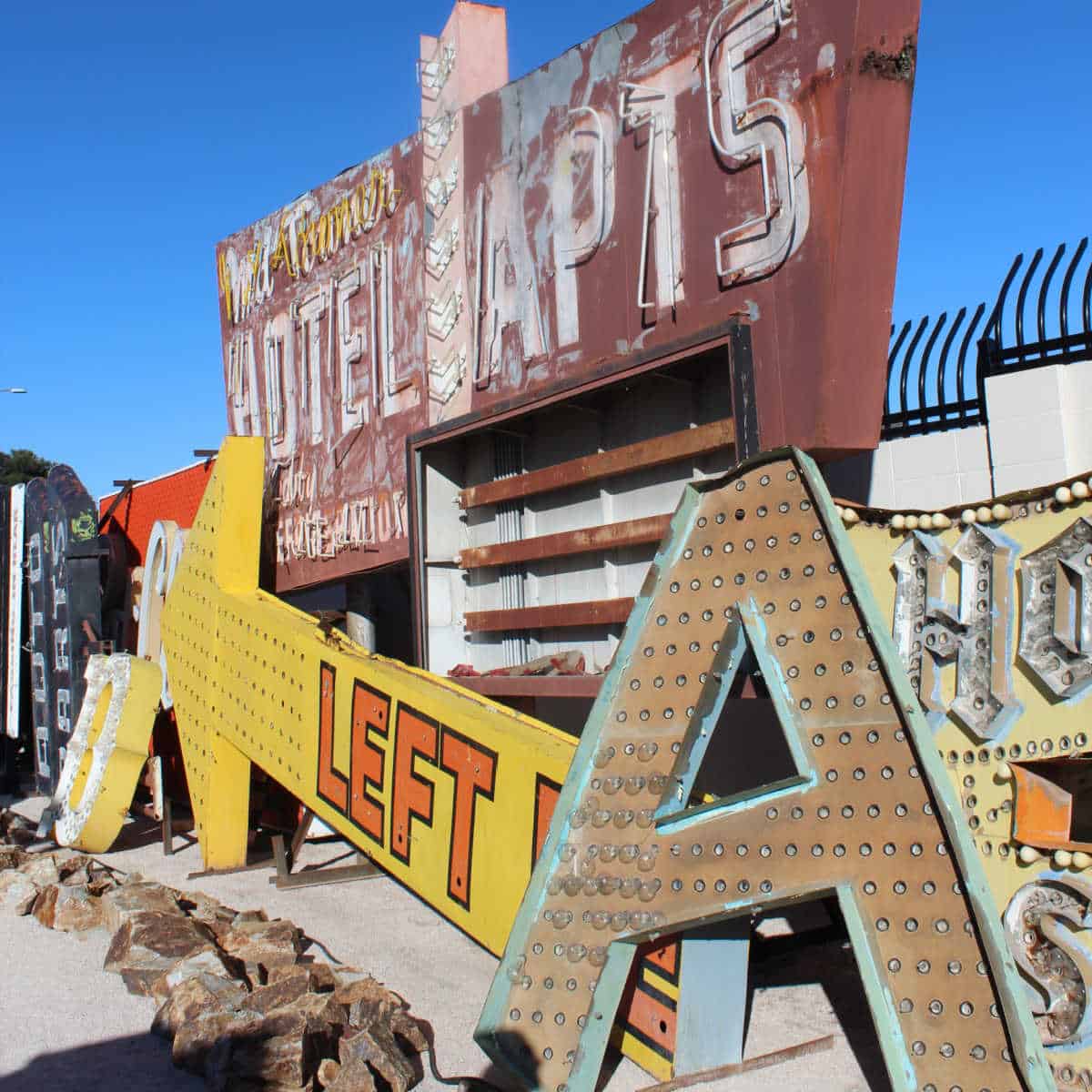 Neon Lights including a yellow left arrow, A, and hotel and apt sign piled next to each other