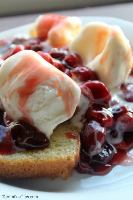 White plate with cherries jubilee on a slice of cake with vanilla ice cream. 
