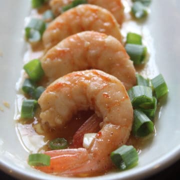 spicy shrimp lined up on a white platter with green onions