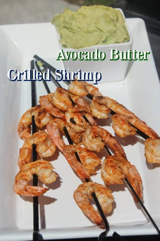 Avocado butter in a white bowl next to shrimp skewers on a white plate