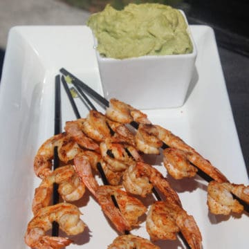 grilled shrimp skewers in front of a bowl of avocado butter