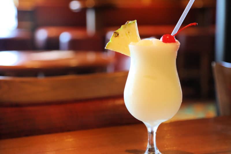 Pina colada in a hurricane glass garnished with a pineapple wedge and maraschino cherry