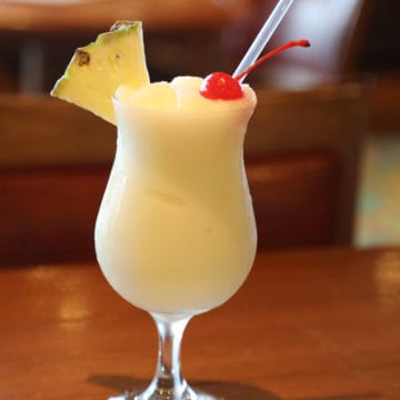 Pina Colada in a hurricane glass with pineapple and cherry garnish