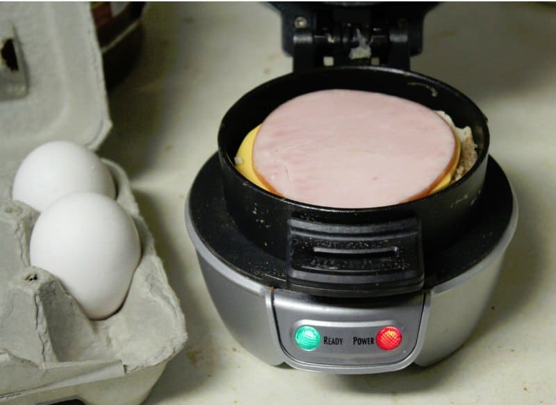 carton of eggs next to a breakfast muffin maker with ham and cheese