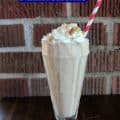 sonic coconut cream pie shake in a clear glass with a pink and white striped straw against a brick background
