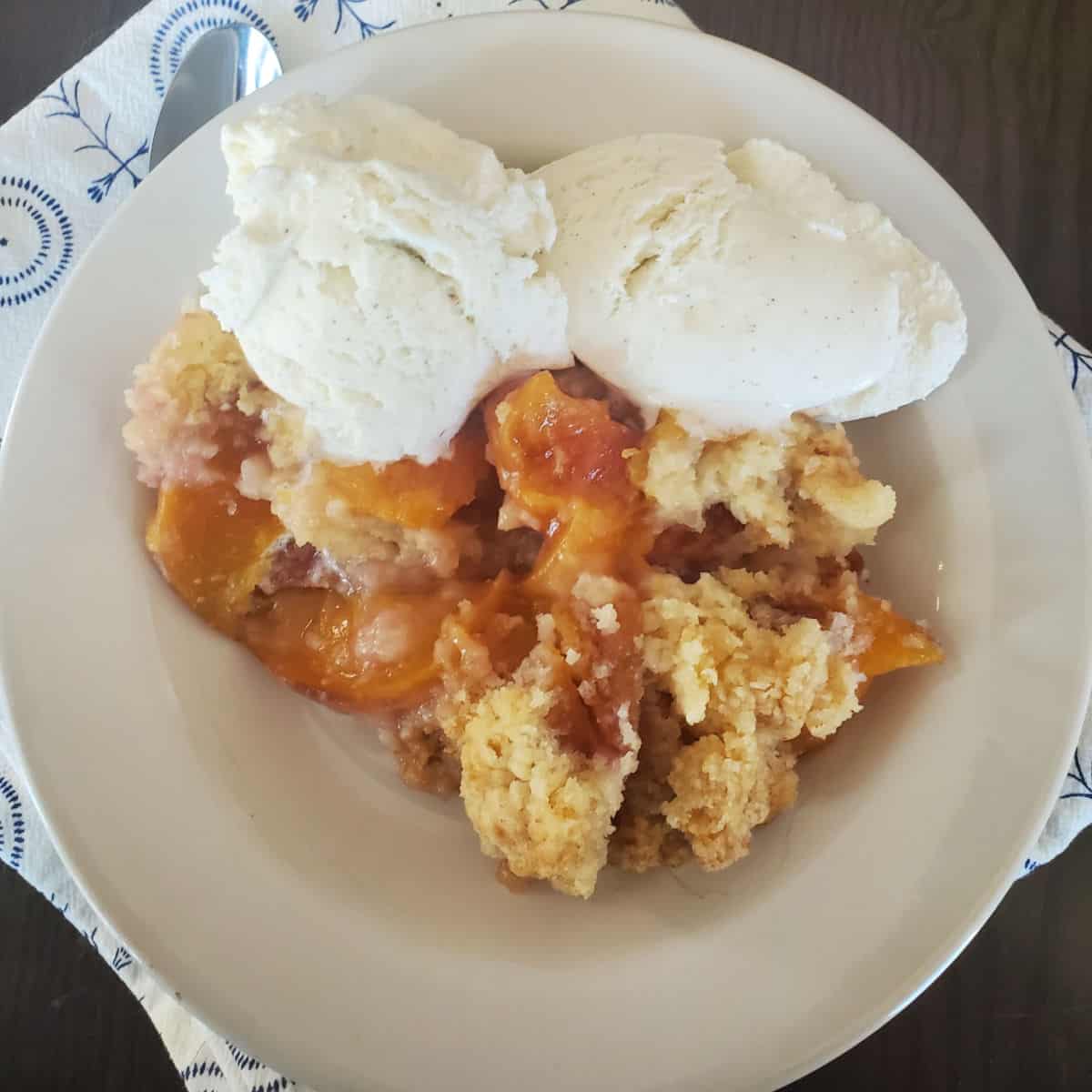 Crock Pot Peach Cobbler with vanilla ice cream in a white bowl