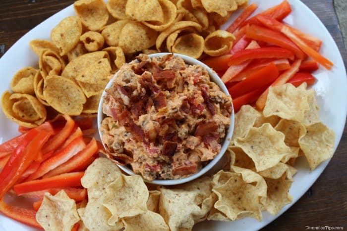 Bacon Cheeseburger Crock Pot Dip in a white bowl surrounded by red bell pepper strips and tortilla chips on a white platter