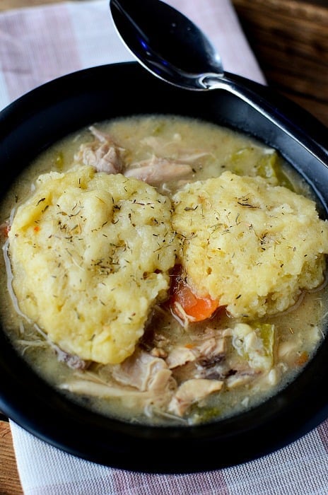 a dark bowl with dumplings on top of chicken