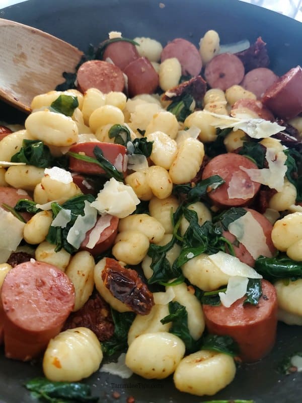 gnocchi, kielbasa, sundried tomatoes, and parmesan cheese in a skillet with a wooden spoon