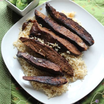 strips of Asian flank steak on a bed of rice on a white plate