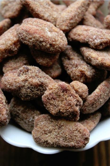 close up of the cinnamon sugar crockpot candied pecans in a white bowl with a brown background. 