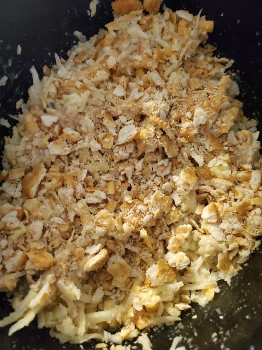 cheesy hashbrown ingredients in a crockpot with crackers on top