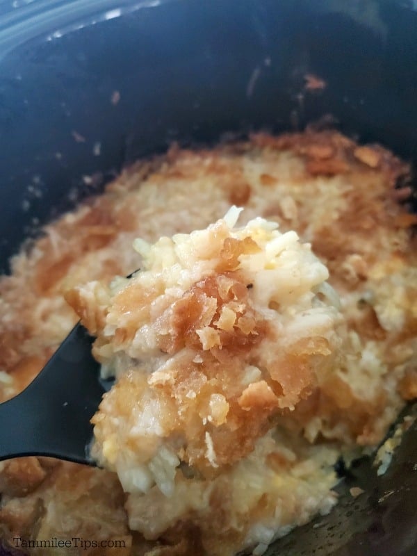 close up of crockpot cheesy hashbrowns on a dark spoon lifting out of the slow cooker
