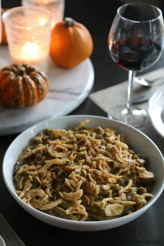 dining table with crockpot green bean casserole, red wine in a glass, candles, and small pumpkins