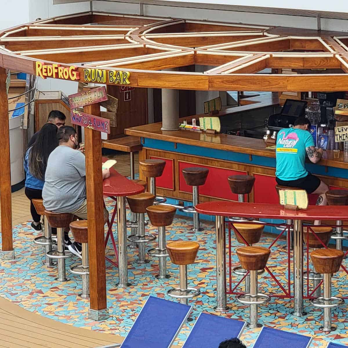 Guests sitting on stools below the RedFrog Rum Bar Sign