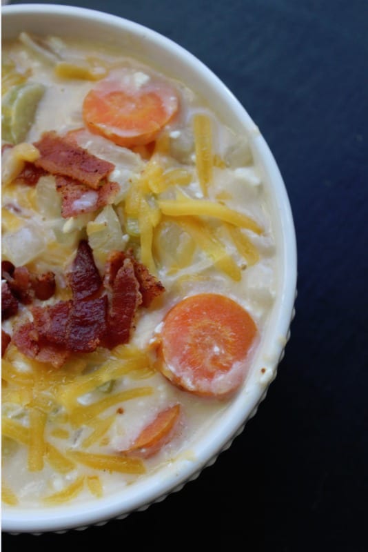 beer cheese soup garnished with bacon and cheese in a white bowl