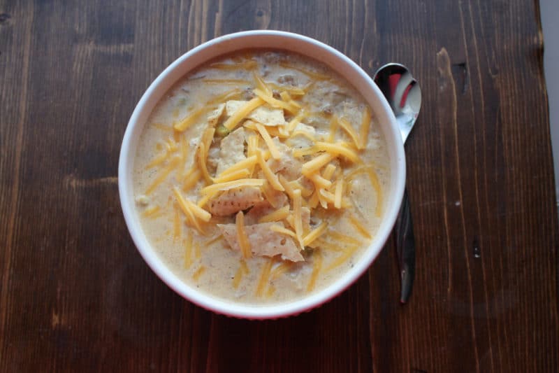 White bowl with soup topped with shredded cheese next to a silver spoon