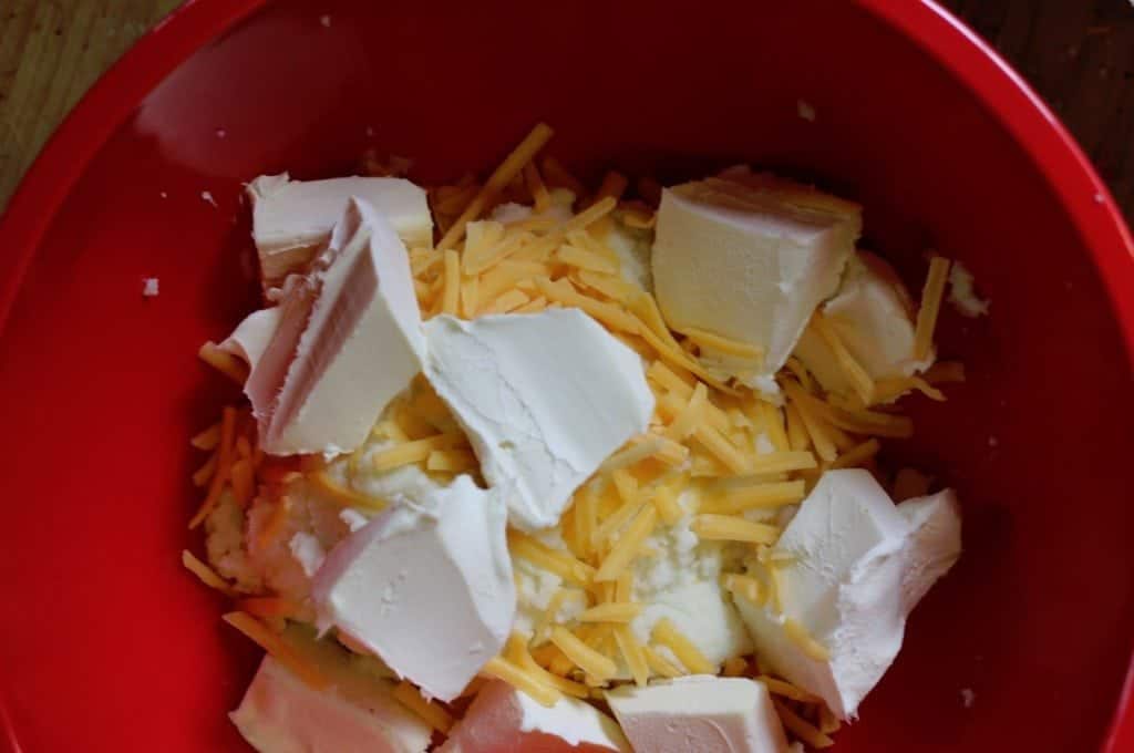 cream cheese and shredded cheese with mashed potatoes in a red bowl