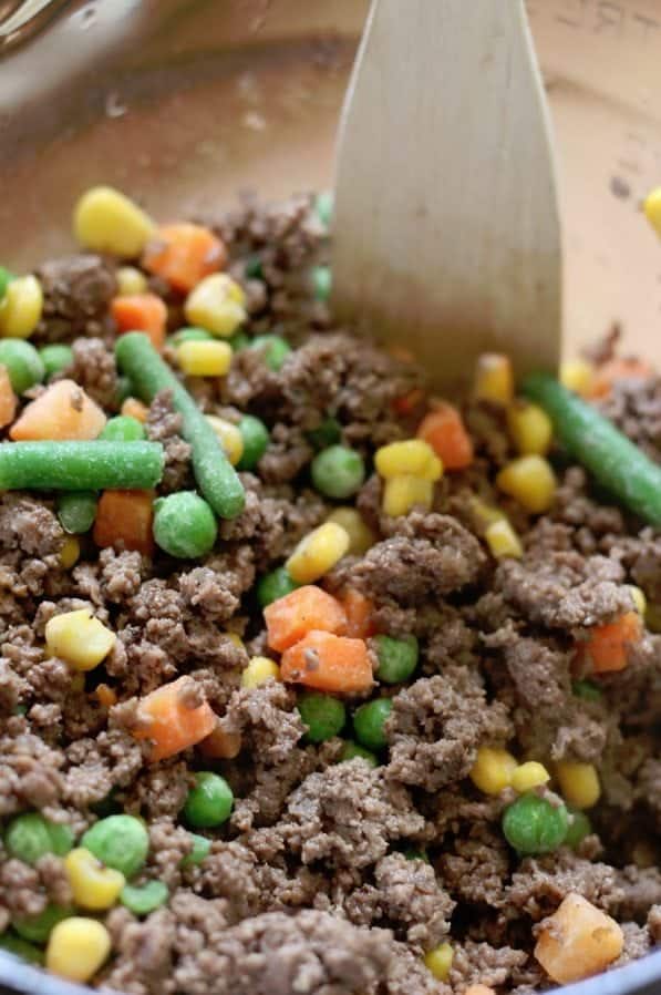 ground beef and mixed vegetables in a glass bowl with a wooden spoon