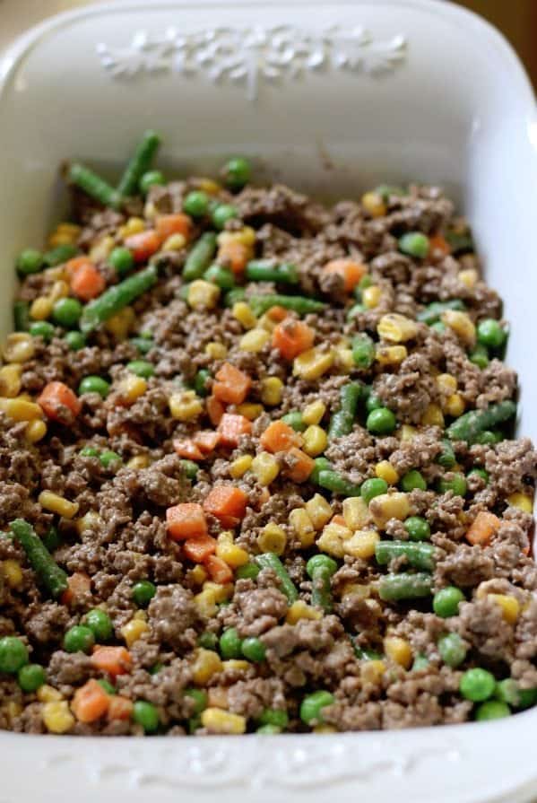 Mixed vegetables and ground beef spread in a white baking dish