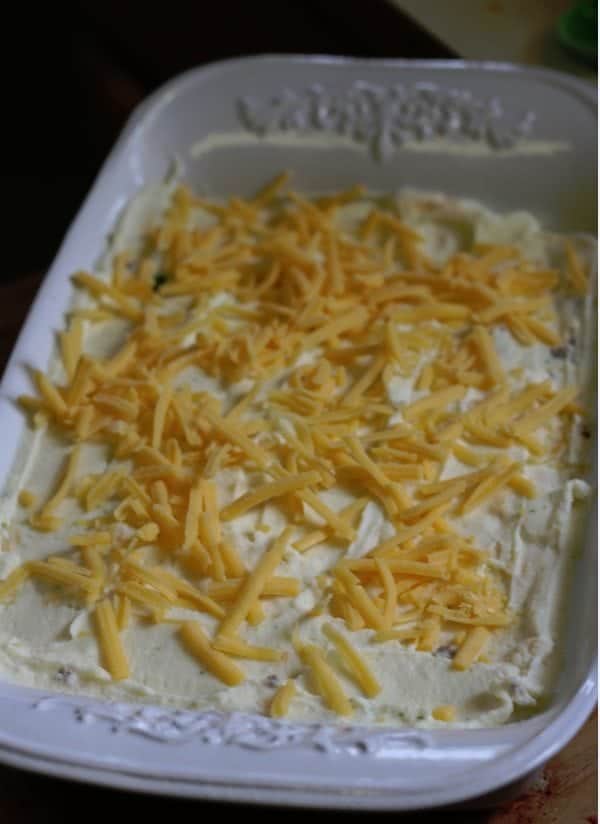 shredded cheddar cheese over mashed potatoes in a baking dish