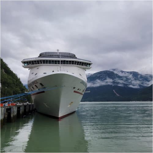 Carnival cruise ship docked with snowy mountains and clouds