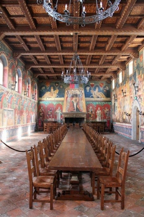 Long wooden tables with a ton of chairs in an ornate room with chandeliers and paintings on the wall