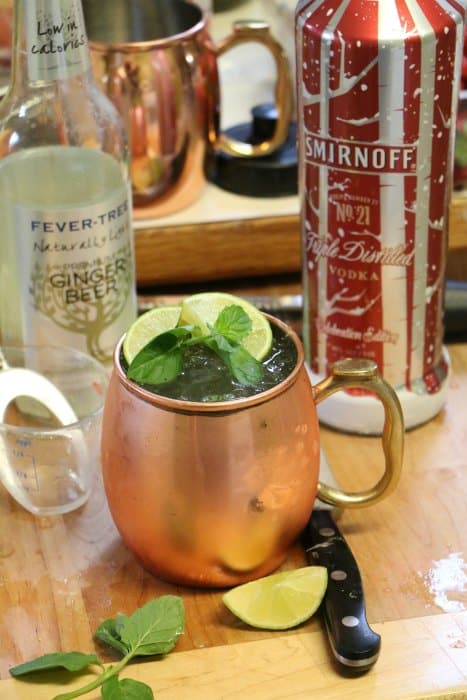 Moscow Mule Cocktail on a cutting board with a bottle of ginger beer and Smirnoff vodka