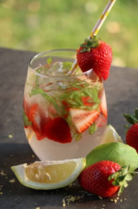 Strawberry basil cocktail in a glass with a sliced lime and strawberries