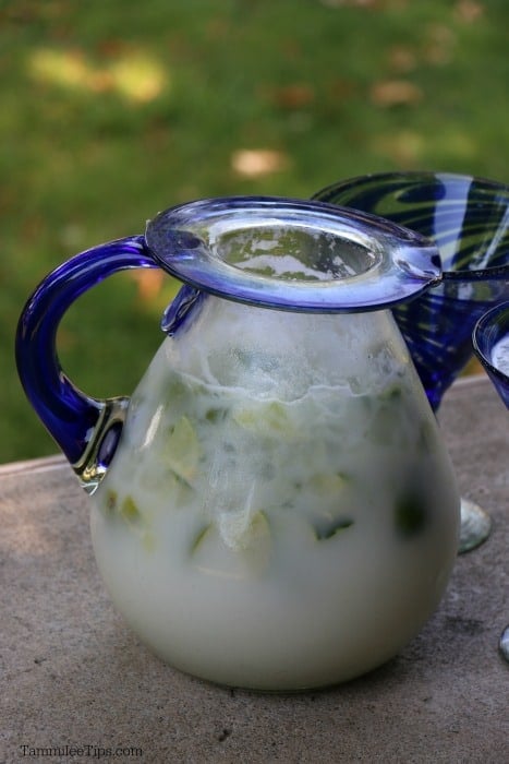 Brazillian lemonade in a glass pitcher with a blue handle. 