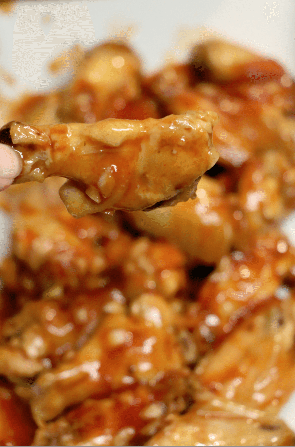 Honey Sriracha coated chicken wing held above a slow cooker