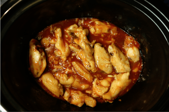 Chicken wings in sauce in a dark slow cooker bowl 