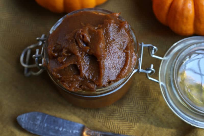 Slow cooker pumpkin butter in a glass jar next to pumpkins and a knife