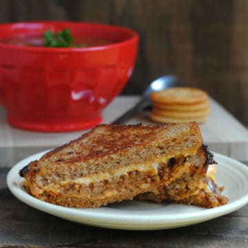 sloppy joe grilled cheese on a white plate next to a bowl of tomato soup
