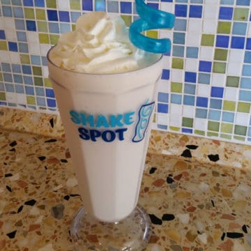 Shake spot glass with a bourbon milkshake with whipped cream garnish and a blue straw