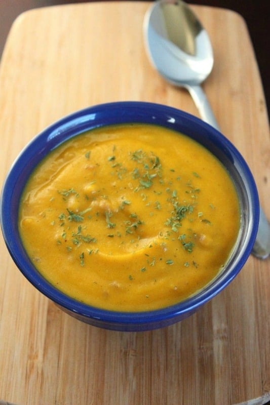 Butternut squash soup in a blue bowl next to a spoon on a cutting board. 