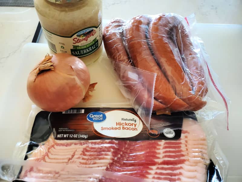 Sauerkraut and pork ingredients, sauerkraut, kielbasa, onion, and bacon on a kitchen counter