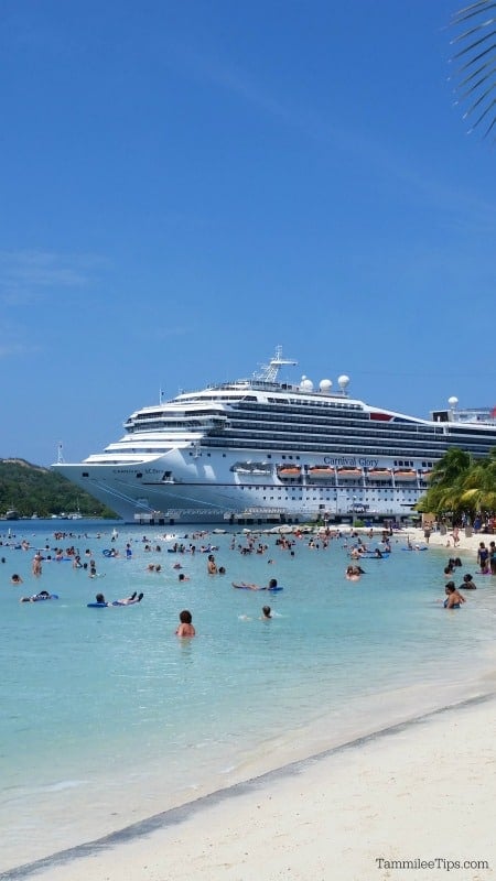 Carnival cruise ship in the background of people playing at the beach and in the water. 