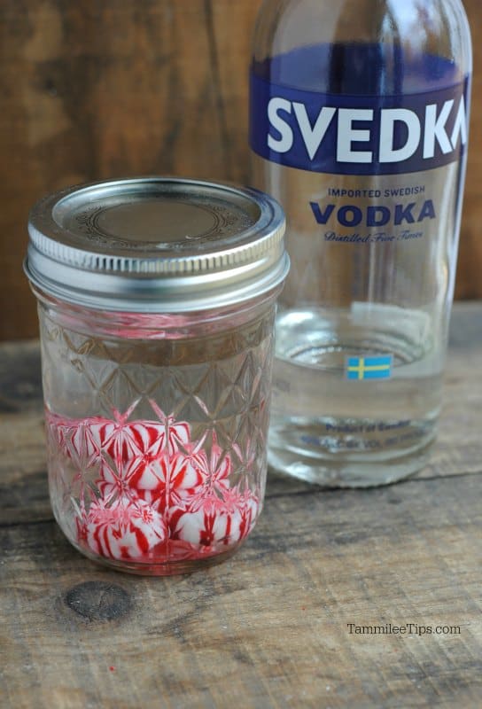 Mason jar with peppermint candies and clear liquid next to a vodka bottle