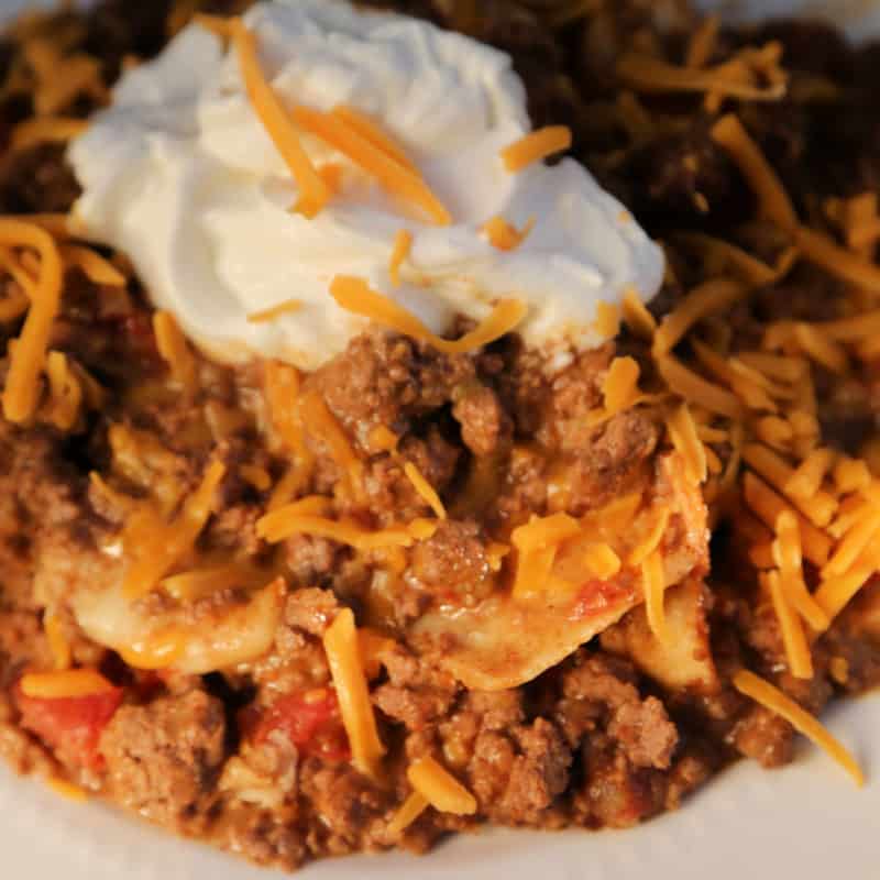 taco beef casserole on a white plate garnished with cheddar cheese and sour cream.