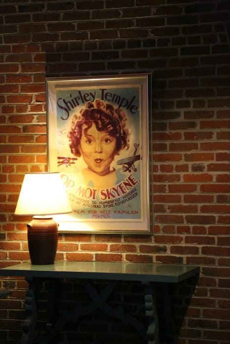 Shirley Temple movie poster above a side table on a brick wall